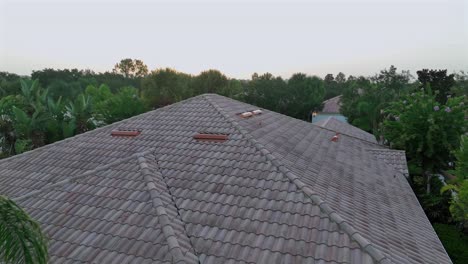 suburban florida home with tiled roof and screened lanai, surrounded by tropical landscaping and palm trees. single-story architecture typical of hurricane-prone coastal areas. aerial approaching
