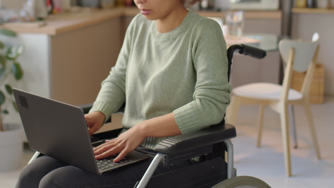 Donna che usa il laptop in sedia a rotelle a casa.