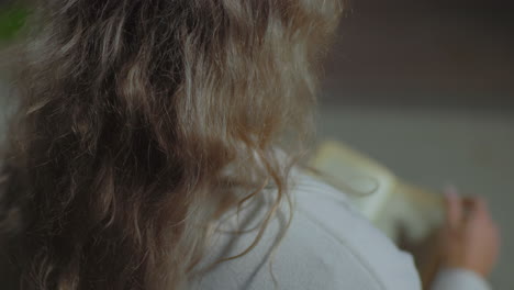 close up rear view of lady seated outdoors at night opening to new page of book in her hand while her curly hair sways softly in wind, creating calm and reflective moment in dimly lit setting