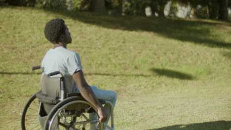 side view of young black man in wheelchair enjoying ride in park