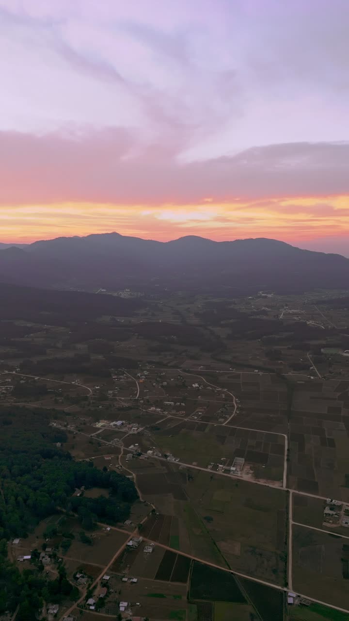 Sunset casts golden light over farmlands and hills in rural Mexican countryside, vertical aerial establishing