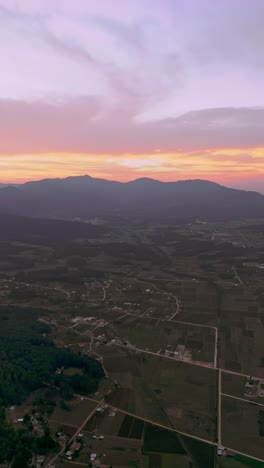 sunset casts golden light over farmlands and hills in rural mexican countryside, vertical aerial establishing