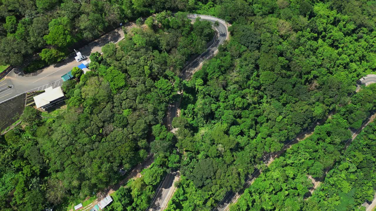 Tilt‑down aerial revealing a winding road through the dense forested slopes of Mt. Samat National Shrine, framed by greenery and hillside terrain in Pilar, Bataan, Philippines
