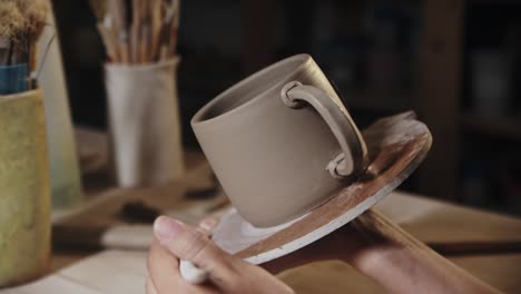 mujer joven poniendo el diseño a una pieza de arcilla en el borde del mango y la copa