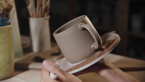 young woman putting on the design to a piece of clay on the edge of the handle and the cup