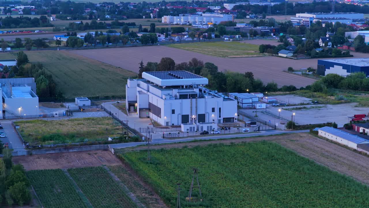 Aerial view of a modern building with solar panels surrounded by fields