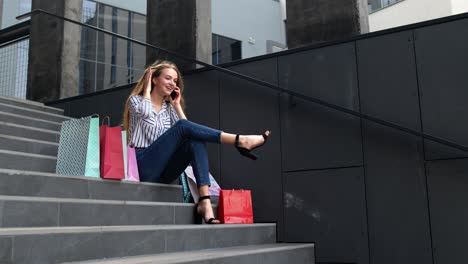 Chica-Sentada-En-Las-Escaleras-Con-Bolsas-Hablando-Por-Teléfono-Móvil-Sobre-La-Venta-En-El-Centro-Comercial-El-Viernes-Negro