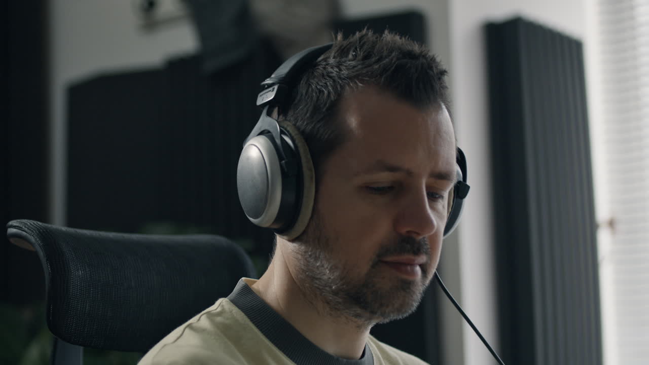 Man listens with headphones while producing audio in acoustically treated home studio