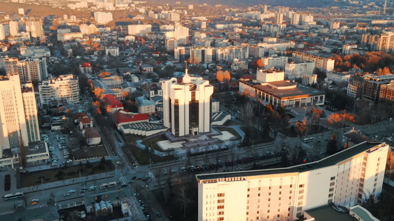 Aerial drone view of Chisinau at sunset. Panorama view of the Presidency and Parliament, multiple buildings in city center, roads with moving cars, bare trees. Moldova