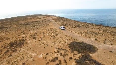 A-lone-4WD-explores-a-rocky-outcrop-by-the-ocean,-180-degree-turn-to-reveal-beautiful-coastline