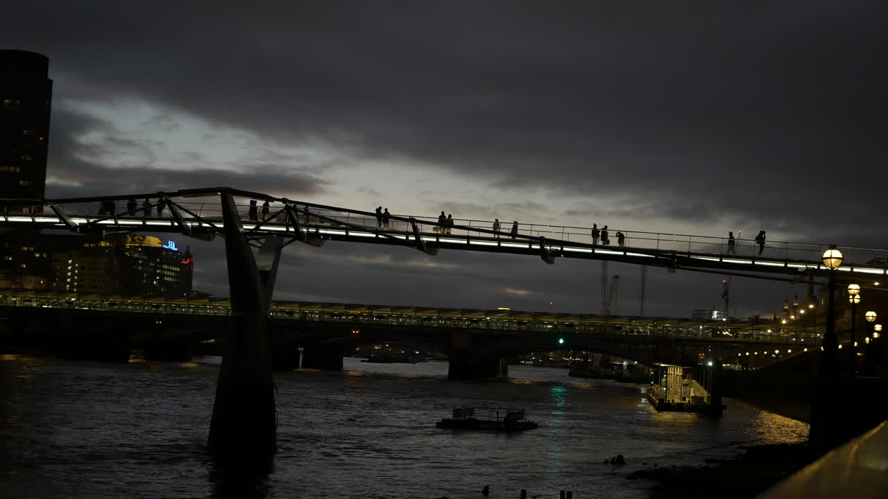 People walk across the Millennium Bridge crossing the River Thames at night in London wide shot