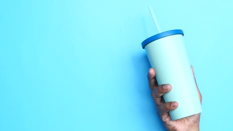 mano sosteniendo un vaso azul claro con una paja