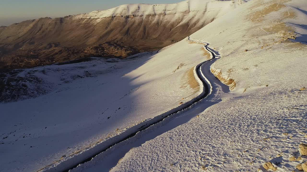 Aerial view in the mountains revealing the snowy road. passing by a lonely shelter during sunset.