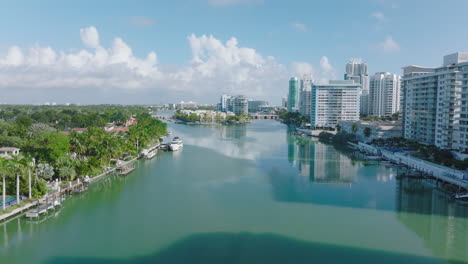 Día-Soleado-En-La-Ciudad,-Hacia-Adelante-Vuela-Sobre-La-Superficie-Del-Agua-Bordeada-Por-Modernos-Edificios-Residenciales-De-Varios-Pisos.-Miami,-Estados-Unidos