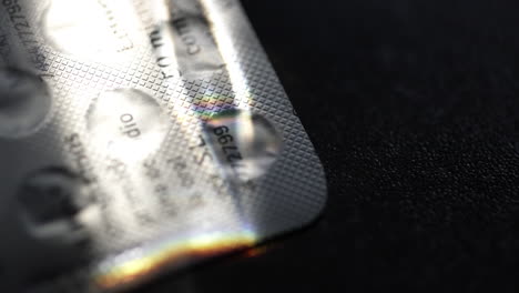 close up of multicolored light rays dancing across pill blister pack surface, casting iridescent reflections against contrasting dark background, highlighting pharmaceutical product details