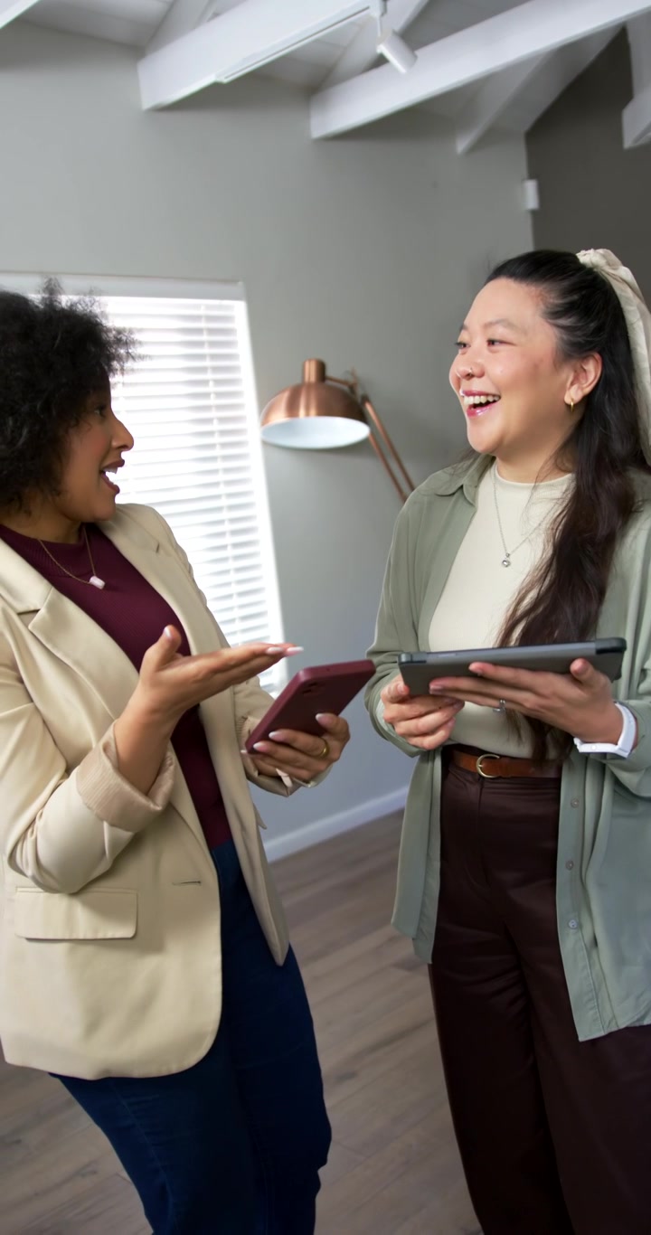 Video verticale: Donne diverse in blazer che toccano il telefono per condividere e rivedono un tablet in ufficio domestico.