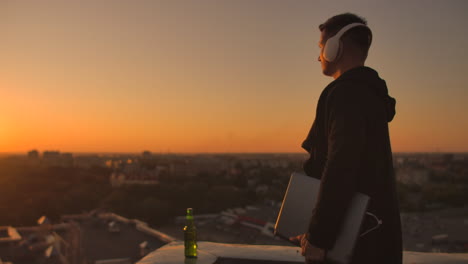 usando un portátil en el techo con vista a la ciudad y gráfico de divisas. concepto de hacking y estadísticas. un hombre al atardecer en cámara lenta escribiendo código de software en un portátil hacker