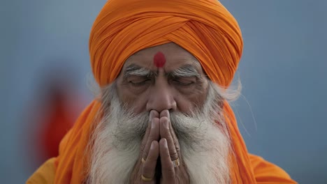 Portrait of a sadhu, a Hindu holy man, wearing an orange turban and traditional clothing, praying with his hands joined in the namaste gesture, eyes closed and a serene expression