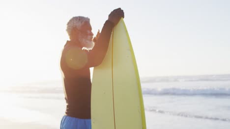 senior african american man holding surfboard on sunny beach