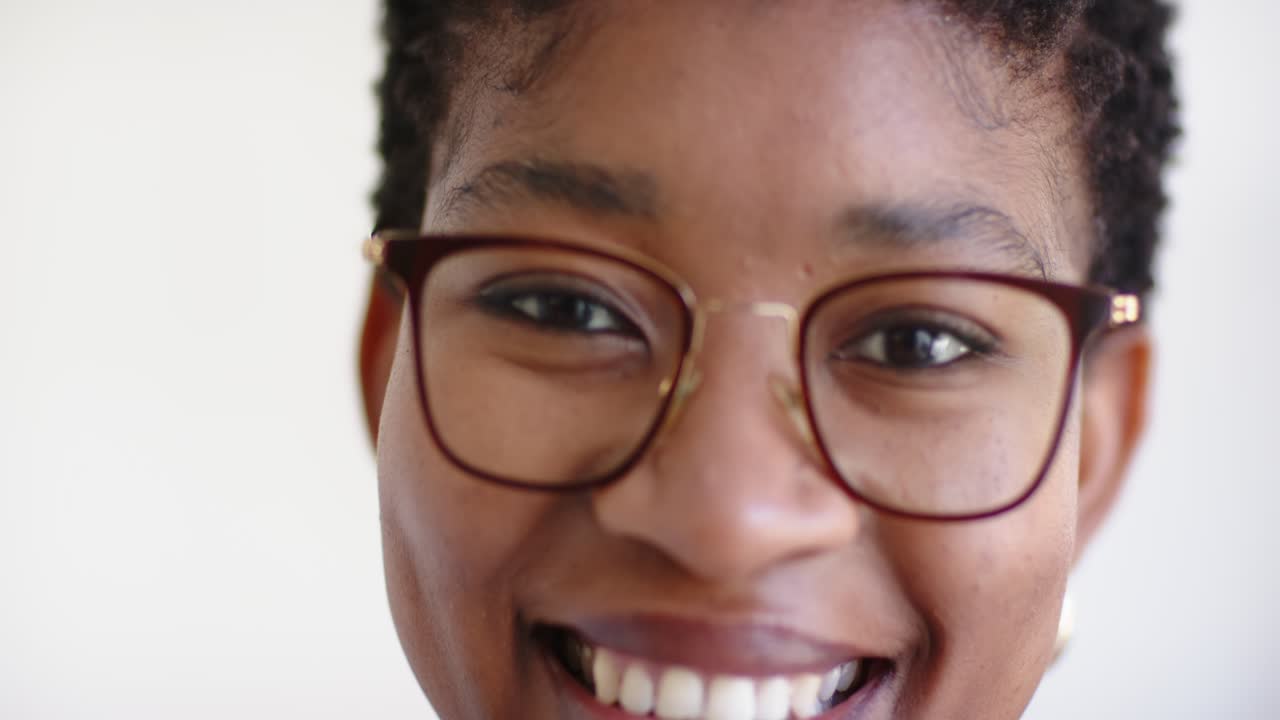 African American woman camera prompt smiling holding gaze at white wall with specs showing warmth