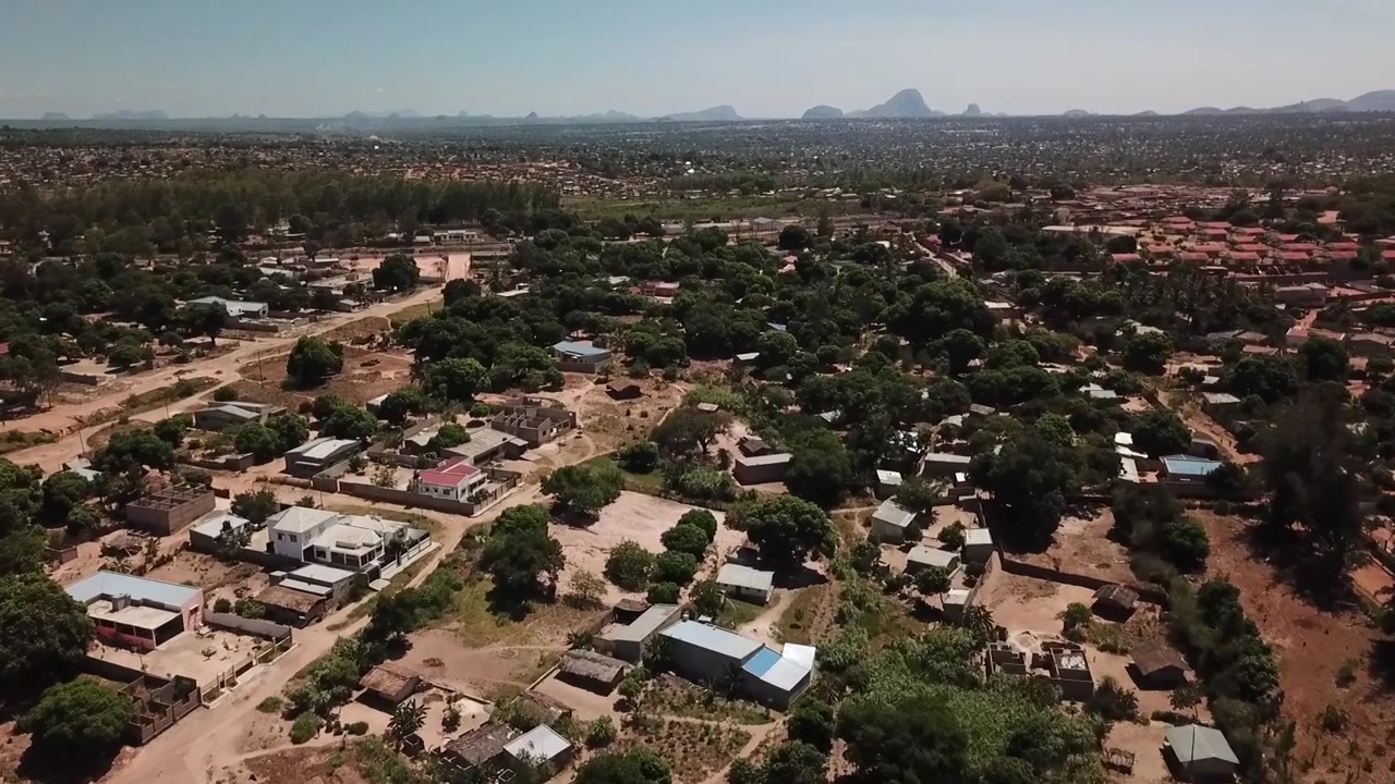 Vista aerea di Nampula, Mozambico, che mostra una densa area urbana con alberi, case, strade polverose e colline distanti.