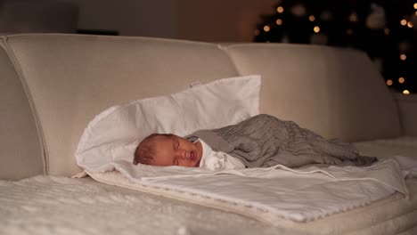 niño recién nacido descansando en el sofá en la sala de estar con el árbol de navidad en el fondo