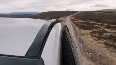 Viaje-Panorámico-Y-Aventurero-A-Través-De-Las-Majestuosas-Tierras-Altas-Escocesas-En-Un-Todoterreno-Plateado,-Con-Una-Vista-Cautivadora-Hacia-El-Largo-Camino-Que-Se-Extiende-A-Través-Del-Vasto-Paisaje-Marrón-En-La-Parte-Trasera