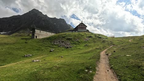 hiking video approaching mountain cabing on a green hill in front of high alpine mountains