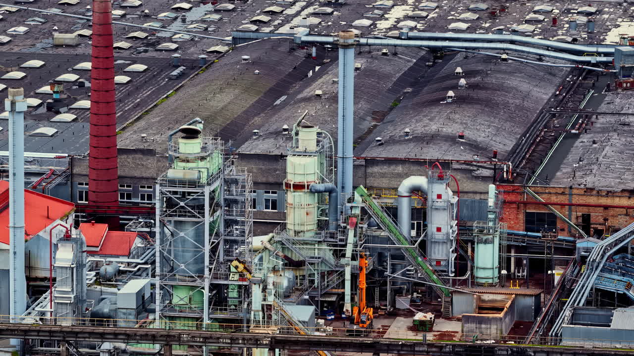 An aerial drone view captures the Bolderaja Ltd industrial complex in Riga, a massive timber and wood processing factory with smokestacks, pipes, and facilities for manufacturing particleboard