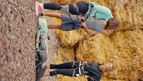 Vertical-video-of-a-girl-with-a-bob-hairstyle,-a-brunette-guy-in-a-gray-T-shirt-and-a-blonde-girl-in-a-black-sports-summer-uniform-attaching-special-equipment-and-insurance-to-their-belt-for-rock-climbing-against-the-backdrop-of-yellow-rocks-that-they-are-going-to-climb