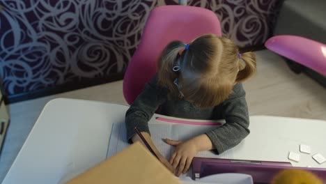 Child-girl-kid-in-medical-mask-doing-school-homework-on-laptop-computer-at-home,-distance-education