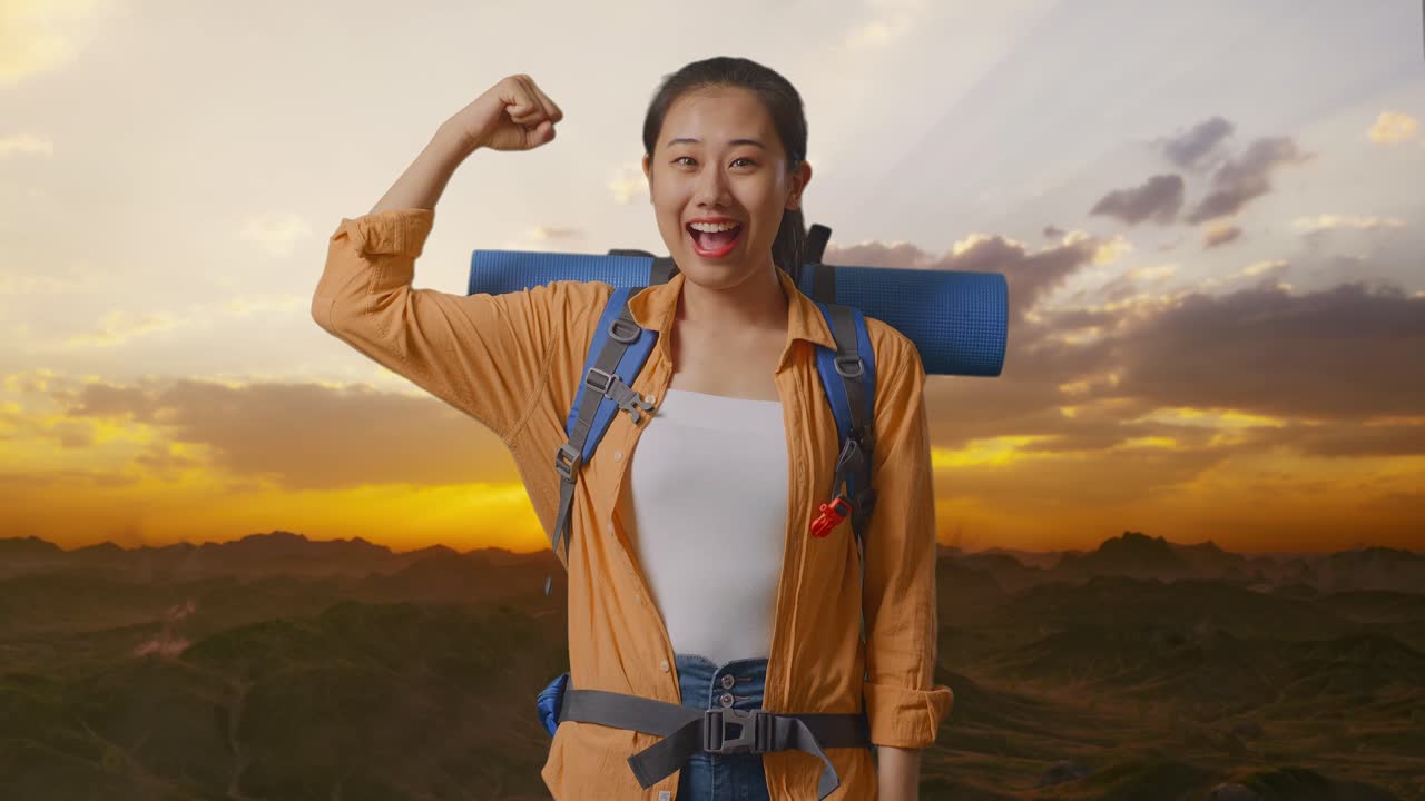 Asian Female Hiker With Mountaineering Backpack Smiling And Flexing Her Bicep While Standing On The Top Of Mountain During Sunset Time