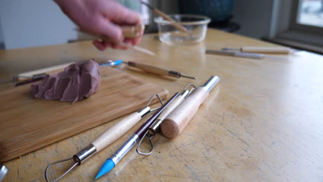 An-artist-begins-to-pack-up-his-tools-and-clean-up-after-sculpting-with-brown-modeling-clay-in-his-messy-art-studio