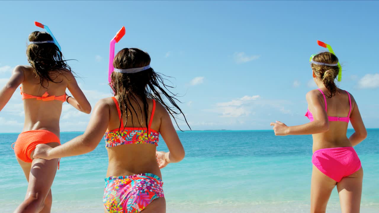 다채로운 수영복을 입은 백인 소녀들이 해변에서 스노클링을 하고 있습니다.