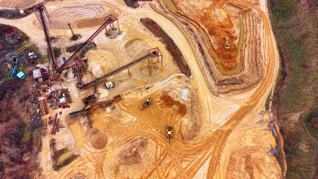 Aerial view of industrial sand quarry mining site with heavy machinery. Top view of sand excavation site featuring yellow machinery, conveyor belts, sand piles, and industrial equipment
