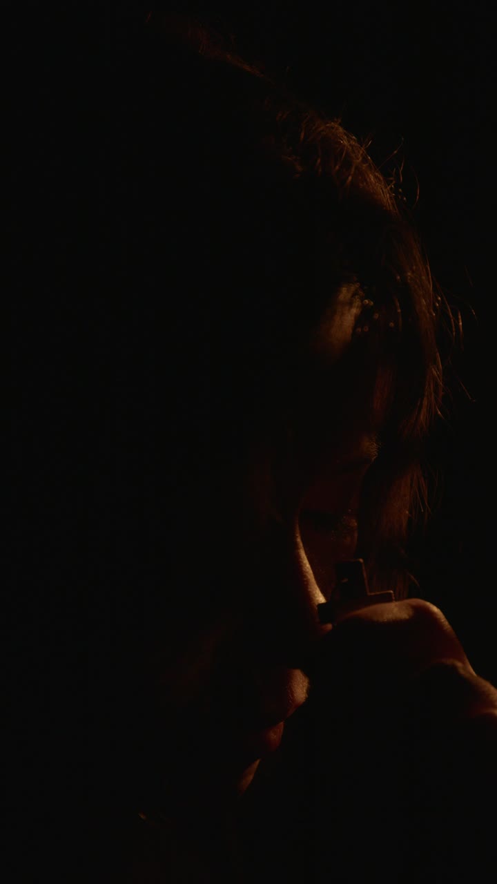Intimate close-up shot of a woman in deep prayer, clutching a cross. The low lighting creates a contemplative and serene atmosphere, perfect for vertical video on social media