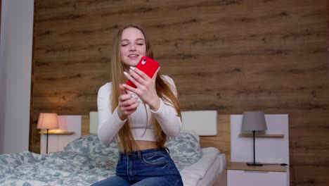 Smiling-cute-vlogger-girl-looking-at-mobile-make-video-call,-shooting-vlog-taking-selfie-at-home