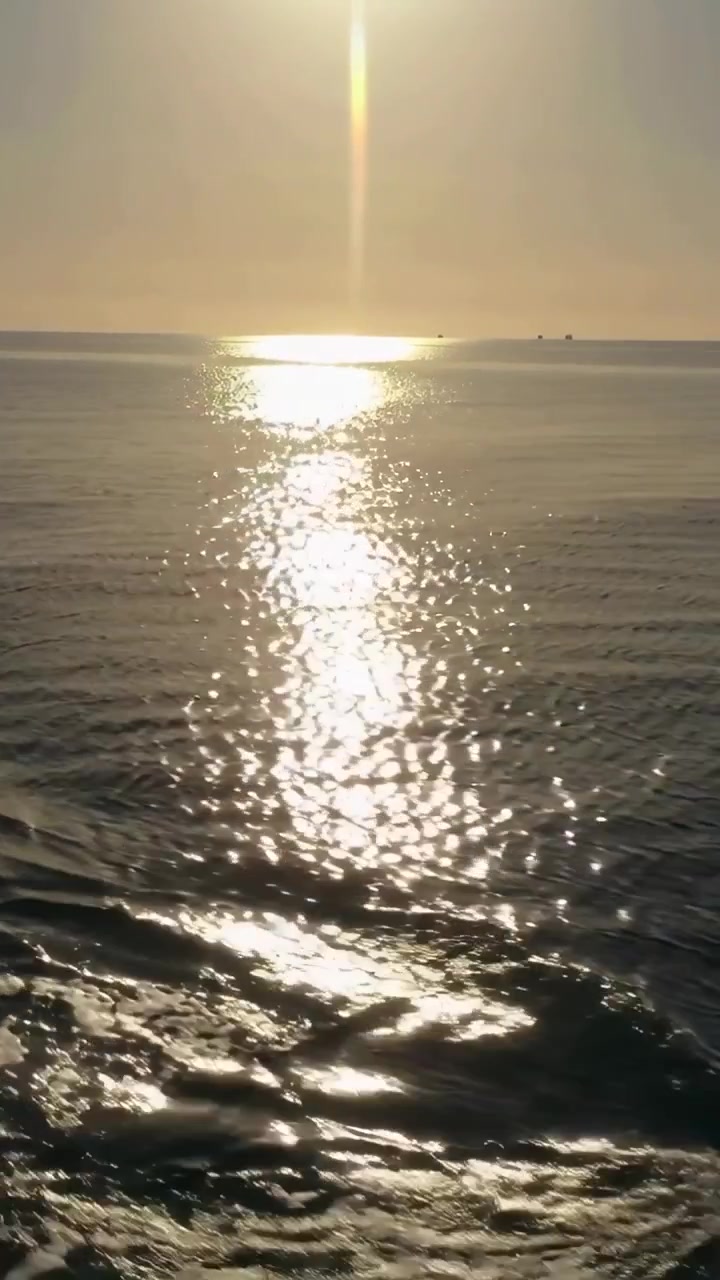 Video vertical: Barco en movimiento creando estela mientras el reflejo del sol brilla en el mar, con embarcaciones.
