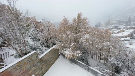 FPV-aerial-drone-flying-over-snow-covered-trees-toward-a-scenic-mountain-village