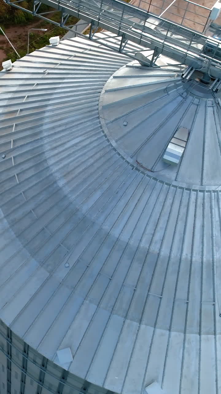 Large storage tank. Modern metal grain elevator on field. Granary for storing and processing agricultural crop. Aerial view. Vertical video