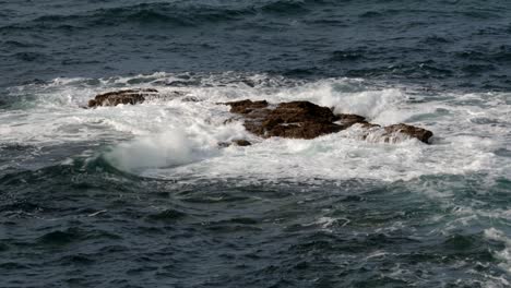 wide-shot-waves-crashing-over-rocks-at-Piskies-Cove-by-HMS-Warspite-monument