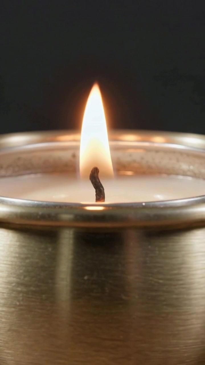 Video verticale: Accensione di una candela in latta metallica con stoppino carbonizzato che prende fuoco dopo il contatto con un fiammifero su un tavolo.
