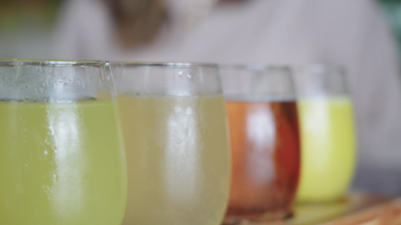 Bir brunch restoranında yemek masasında elma suyu, limonata ve portakal suyu gibi soğuk renkli meyve sularının bardaklarda servis edildiği 4K yakın çekim görüntüler