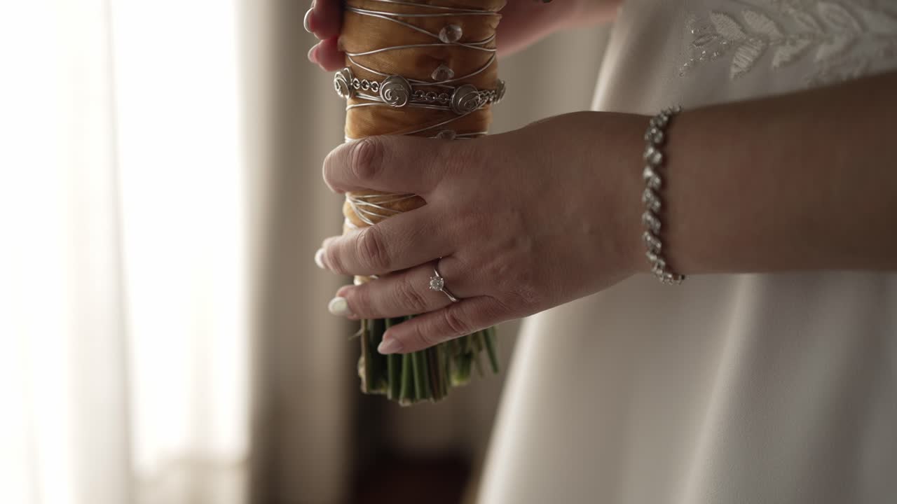 Sposa che tiene un bouquet, mostrando il suo anello di fidanzamento e il braccialetto, pronta per la cerimonia.