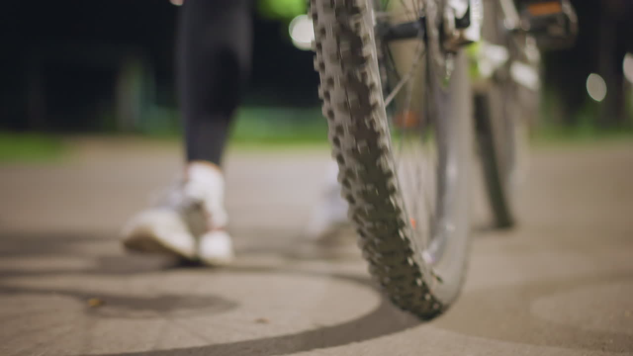 Nighttime Park Pathway Illuminated With Soft Lighting And Cyclist Preparing To Ride, Peaceful Evening Scene Showing Cyclist Ready To Ride Along Lit Park Pathway With Shoes And Bike Details