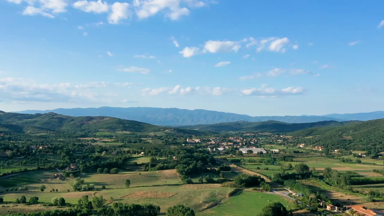 Drone hyperlapse of a green valley in Tuscany with woods, hills, fields, mountains and blue sky.
