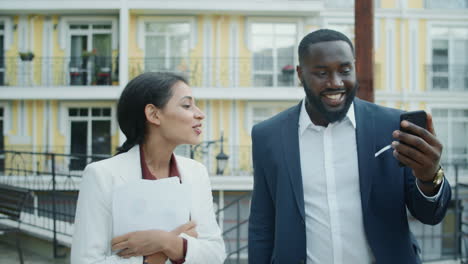 joyful mixed race couple waving hands during video chat outside. team walking