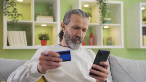 Elderly-man-sitting-on-sofa-at-home-with-credit-card-shopping-online.