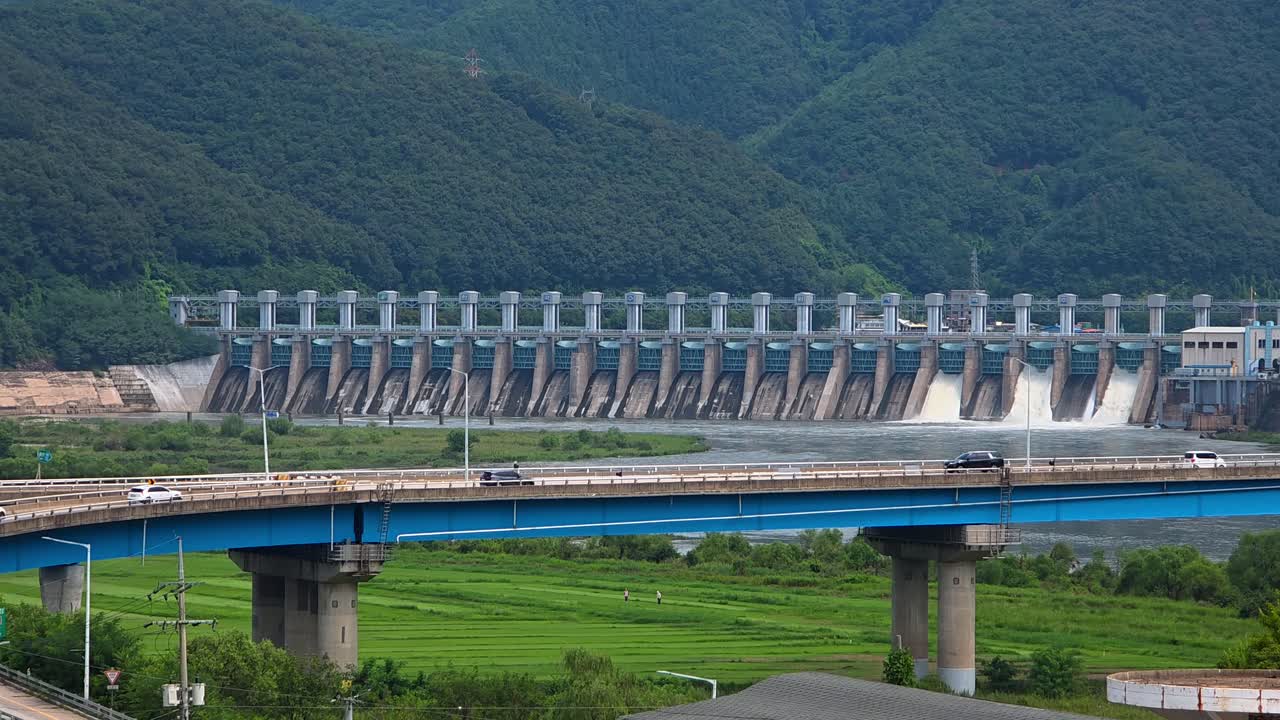 View of car traffic crossing the New Cheongpyeong Bridge over the Bukhan River with the massive Cheongpyeong hydroelectric dam in the mountain landscape