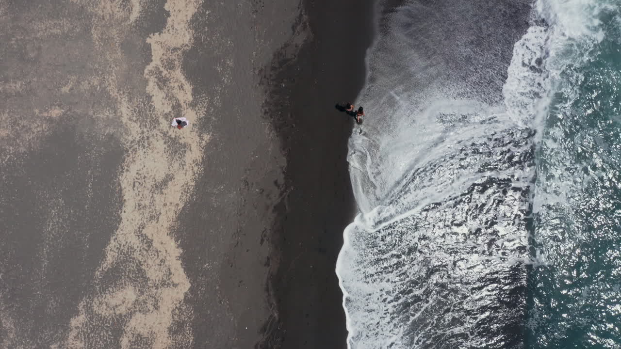 Aerea: Ripresa dall'alto a seguire di due bambini che camminano sulla spiaggia di Vlychada a Santorini, Grecia